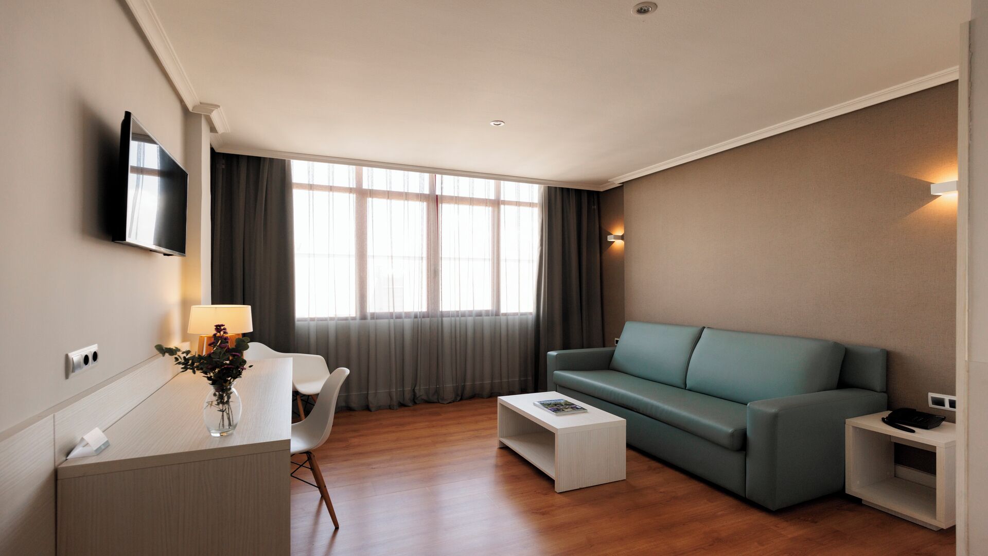 Una sala de estar moderna con una televisión de pantalla plana montada en la pared, un sofá, una mesa de centro y un escritorio con una lámpara.