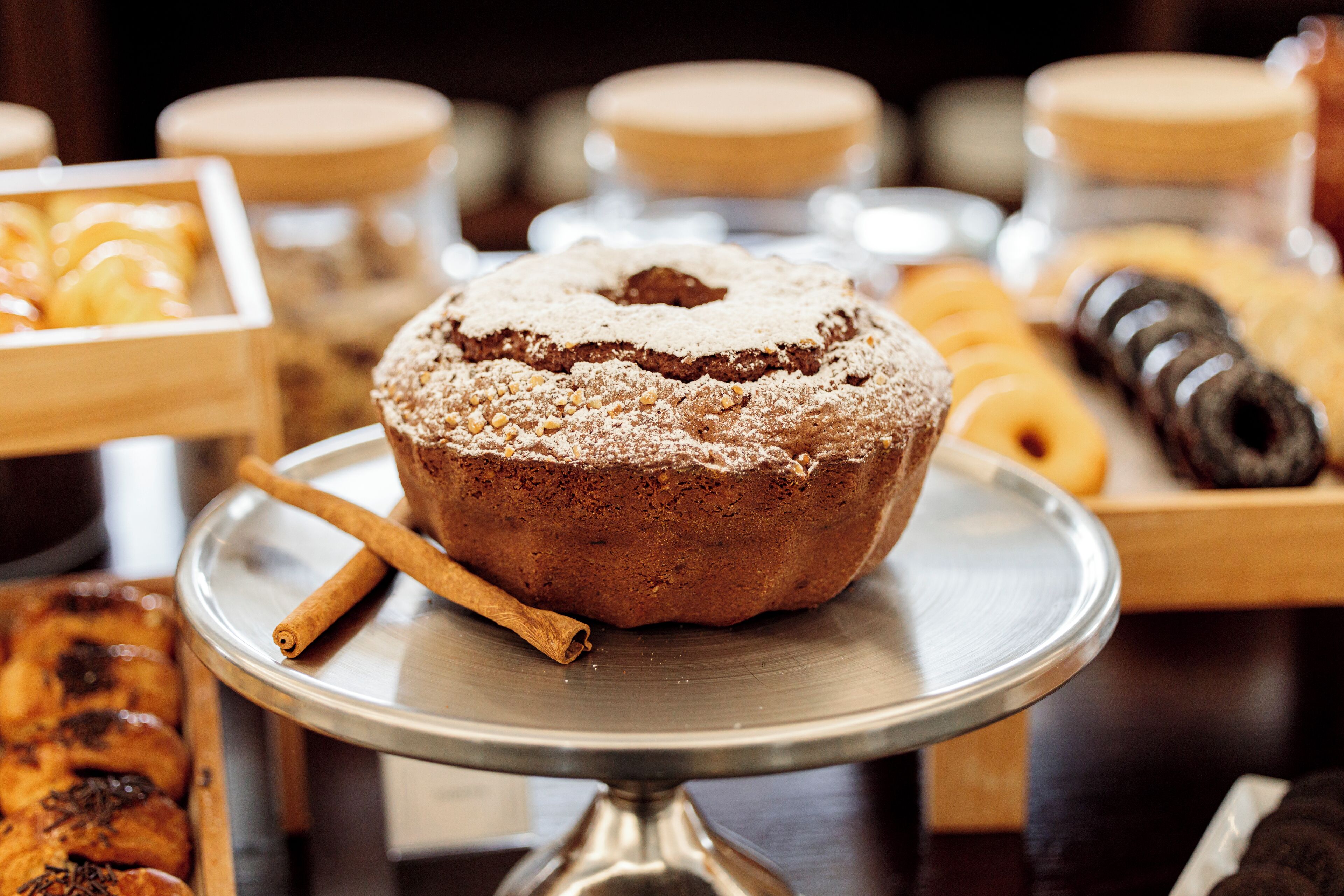 A cake on a metal stand with a cinnamon stick beside it.