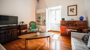 Un salon avec un plancher en bois, un téléviseur, un fauteuil vert, un meuble blanc, un piano et un canapé.