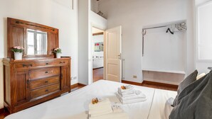Une chambre avec une commode en bois, un lit où les serviettes sont soigneusement pliées, et une salle de bain équipée d’un porte-serviettes.