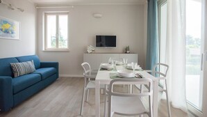Un soggiorno moderno con un divano blu, un tavolo da pranzo per quattro persone e una TV fissata alla parete.