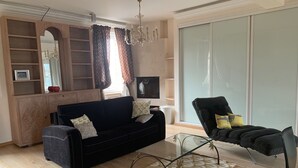 A living room with a dark blue sofa, a glass coffee table, a black armchair, and a patterned rug. - Beautiful 1Bd Duplex close to the Pétrusse and the City Historical center (Luxembourg)