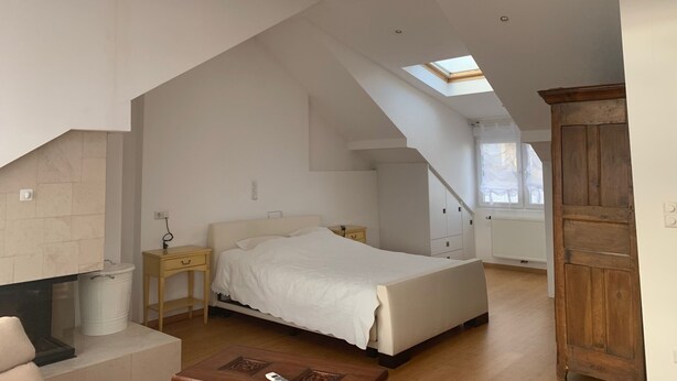 A bedroom with a sloped ceiling, skylight, a bed, a nightstand, a wooden wardrobe, and a fireplace. - Beautiful 1Bd Duplex close to the Pétrusse and the City Historical center (Luxembourg)