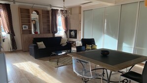 A modern living room with a sofa, a dining table with chairs, and a large window with curtains. - Beautiful 1Bd Duplex close to the Pétrusse and the City Historical center (Luxembourg)