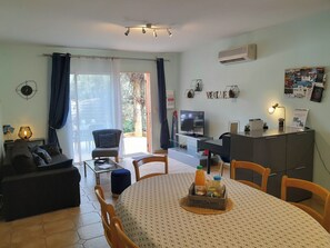 Un salon moderne comprenant un canapé, une table à manger avec un set de table, un téléviseur et un bureau avec une lampe.