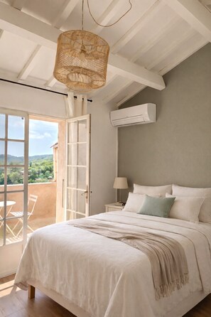 A bedroom with a bed, a hanging light fixture, an air conditioning unit, and a view through a glass door.