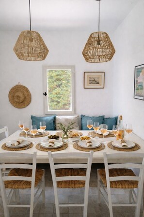 A dining area with a white table set for four, featuring woven placemats, white plates, and glasses of wine.