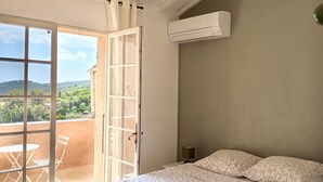 Un dormitorio con cama, una lámpara colgante de mimbre, unidad de aire acondicionado y un balcón con mesa y sillas.