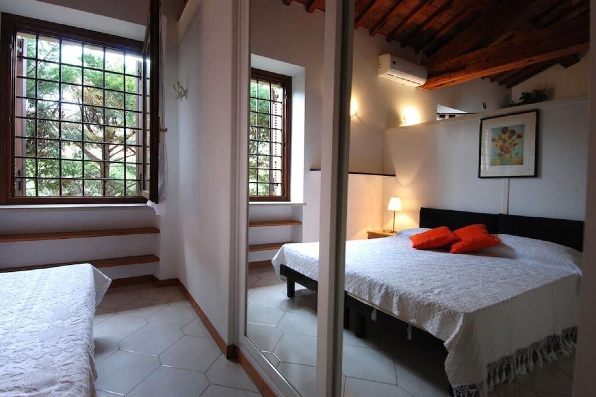 Quarto com uma cama, mesa de cabeceira e janela com vista para árvores.