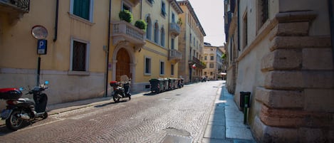 Calle adoquinada flanqueada por edificios históricos, una scooter estacionada y botes de basura.
