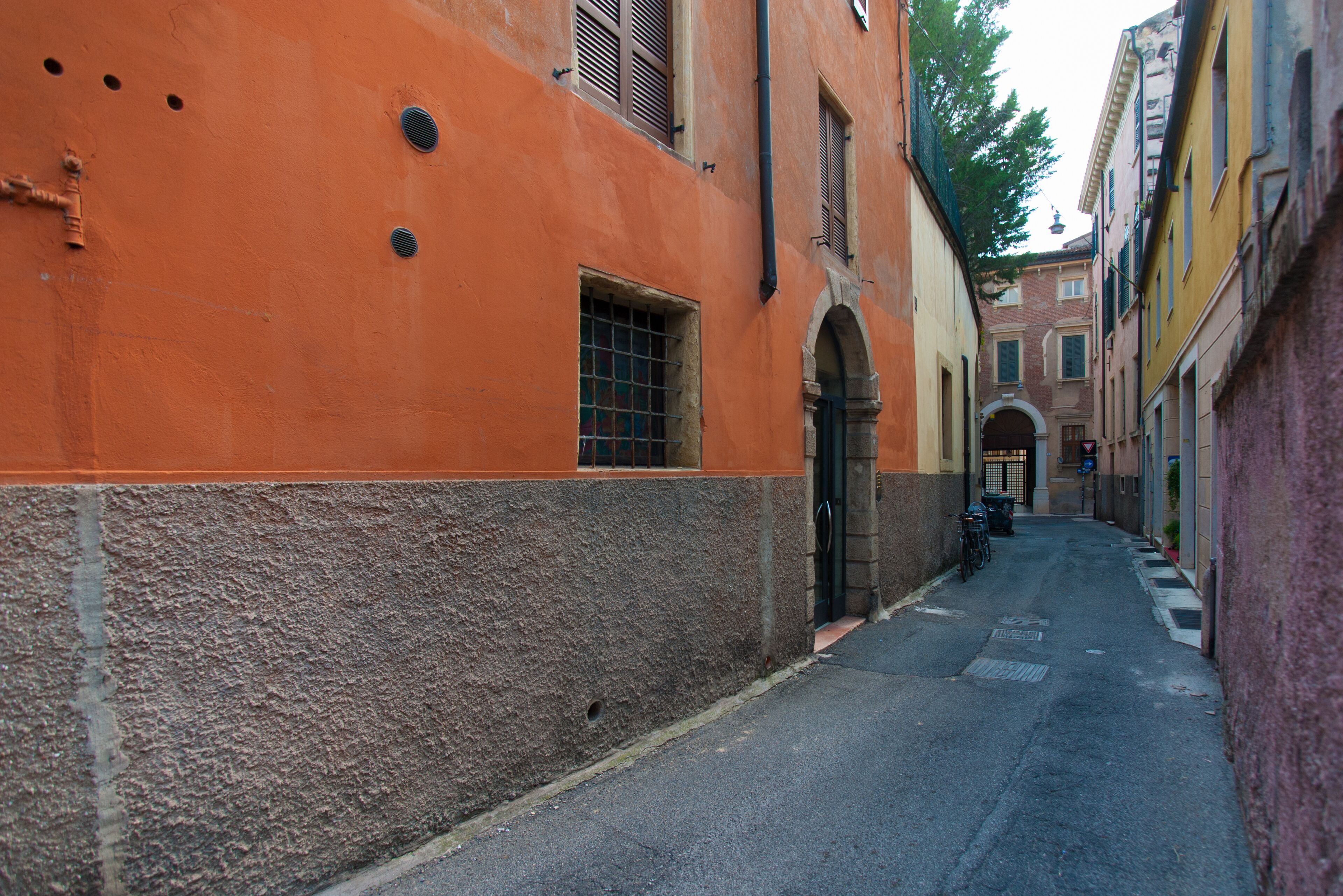 A narrow street with buildings on either side, featuring an orange building with a window and a door.
