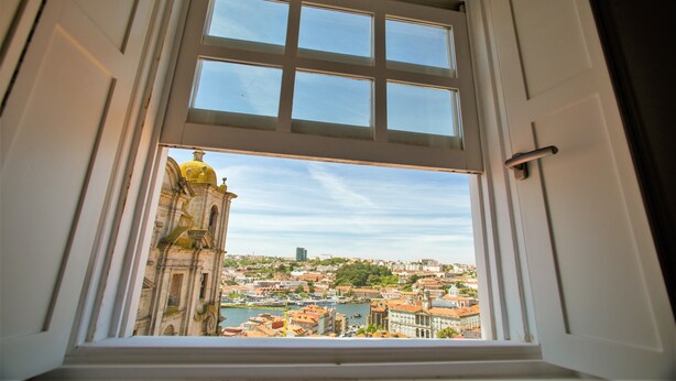 Visão através de uma janela aberta, mostrando um edifício histórico com cúpula e um rio.