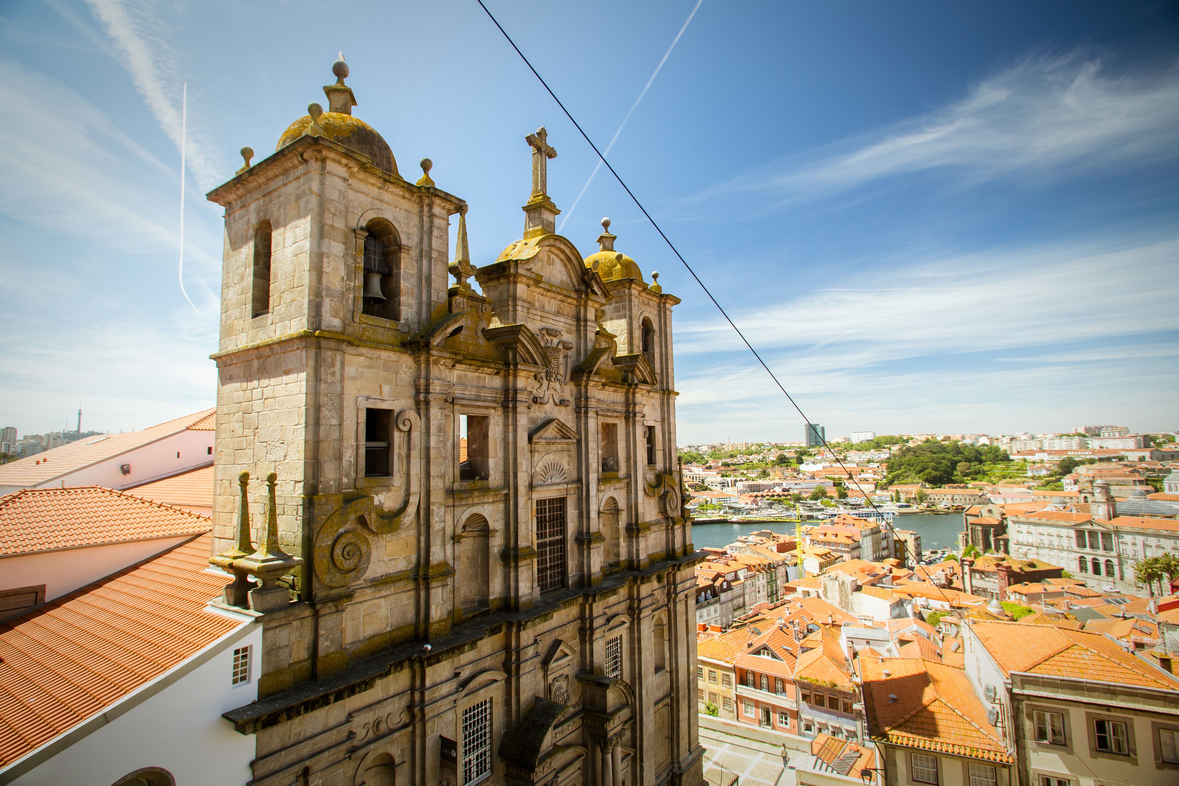 Eine historische Kirche mit einem Glockenturm, mit Blick auf eine Stadtlandschaft mit roten Dächern und einem Fluss.