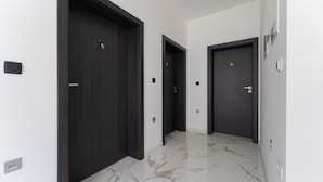 A hallway with three dark wooden doors, each marked with a number. The floor is tiled with white marble. - Sky & Sun Luxury Rooms (Zadar)