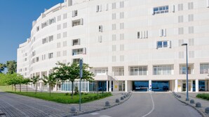 A modern multi-story building with a curved facade, large windows, and a central entrance with a blue car parked inside. - Sky & Sun Luxury Rooms (Zadar)