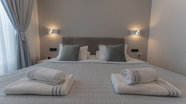 A neatly made double bed with a quilted headboard, two bedside lamps, and two rolled towels on the bed. - Sky & Sun Luxury Rooms (Zadar)