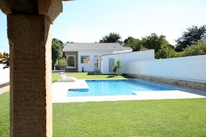 A modern house with a swimming pool, a stone pillar, and a well-maintained lawn.