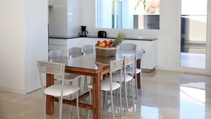 A modern kitchen with a glass dining table, white chairs, and a fruit basket. - Private house in Viña de Millán (O Grove)