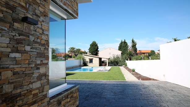 A modern house with a stone exterior, a swimming pool, and a paved patio area. - Private house in Viña de Millán (O Grove)
