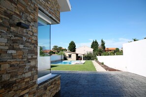 Une maison moderne avec une façade en pierre, une piscine et une terrasse dallée.