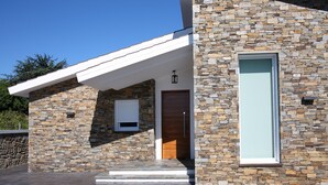 A modern building with a stone facade, a wooden door, and a large window. - Private house in Viña de Millán (O Grove)