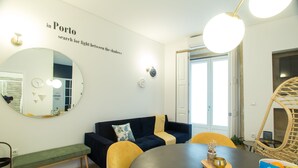 A modern room with a round mirror, a dark blue sofa, yellow chairs, a wooden bench, a round table with a placemat, and a welcome sign. - Janelas de São Bento by Porto City Hosts (Porto)