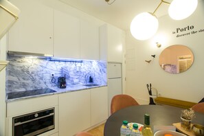 A modern kitchen with white cabinets, a marble countertop, and a built-in oven. There is a dining area with a round table and chairs. - Janelas de São Bento by Porto City Hosts (Porto)
