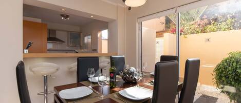 Un comedor con una mesa dispuesta para cuatro, una lámpara colgante moderna y vistas a un jardín a través de un ventanal.