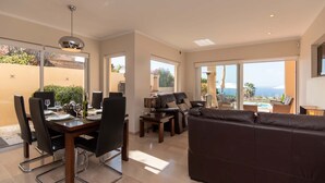 Amplia sala de estar con una mesa de comedor para cuatro, un sofá y vistas al exterior.
