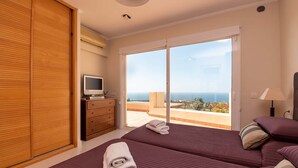 Un dormitorio con dos camas, televisión y balcón con vistas al mar.