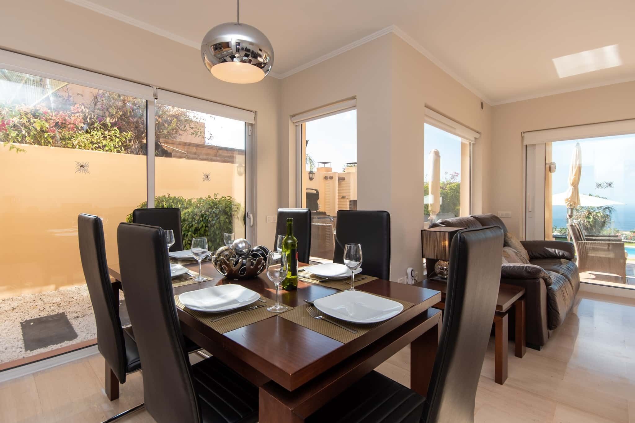 Un comedor con una mesa dispuesta para cuatro, sillas, una lámpara colgante y vistas al exterior.