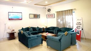 A living room with two sofas, a coffee table, a TV, and a poster. - Royalton Inn Hotel (Lahore)