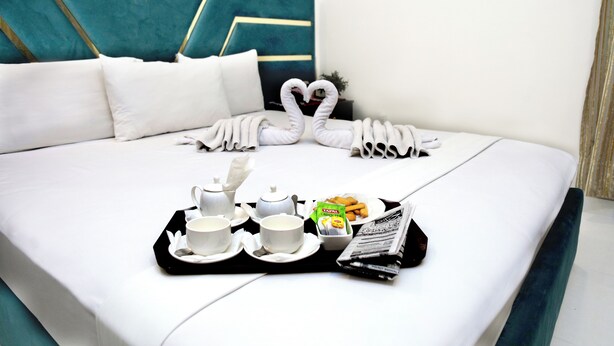 A neatly made bed with a tray of breakfast items including cups, a teapot, and a box of cereal. - Royalton Inn Hotel (Lahore)