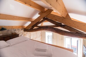 A bedroom with a wooden ceiling structure, a bed with white linens, a nightstand, and a stone wall. - Picasso Suites Porto by Porto City Hosts (Porto)