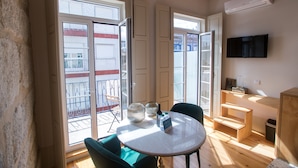 A room with a round table, chairs, and a TV mounted on the wall. There are open doors leading to an outdoor area with a balcony. - Picasso Suites Porto by Porto City Hosts (Porto)
