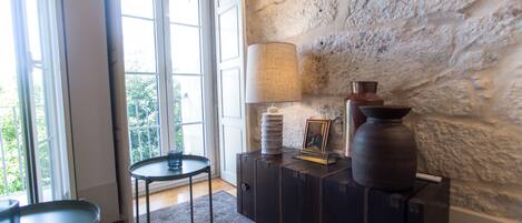 Una habitación con pared de piedra, una lámpara, un jarrón y una mesita.