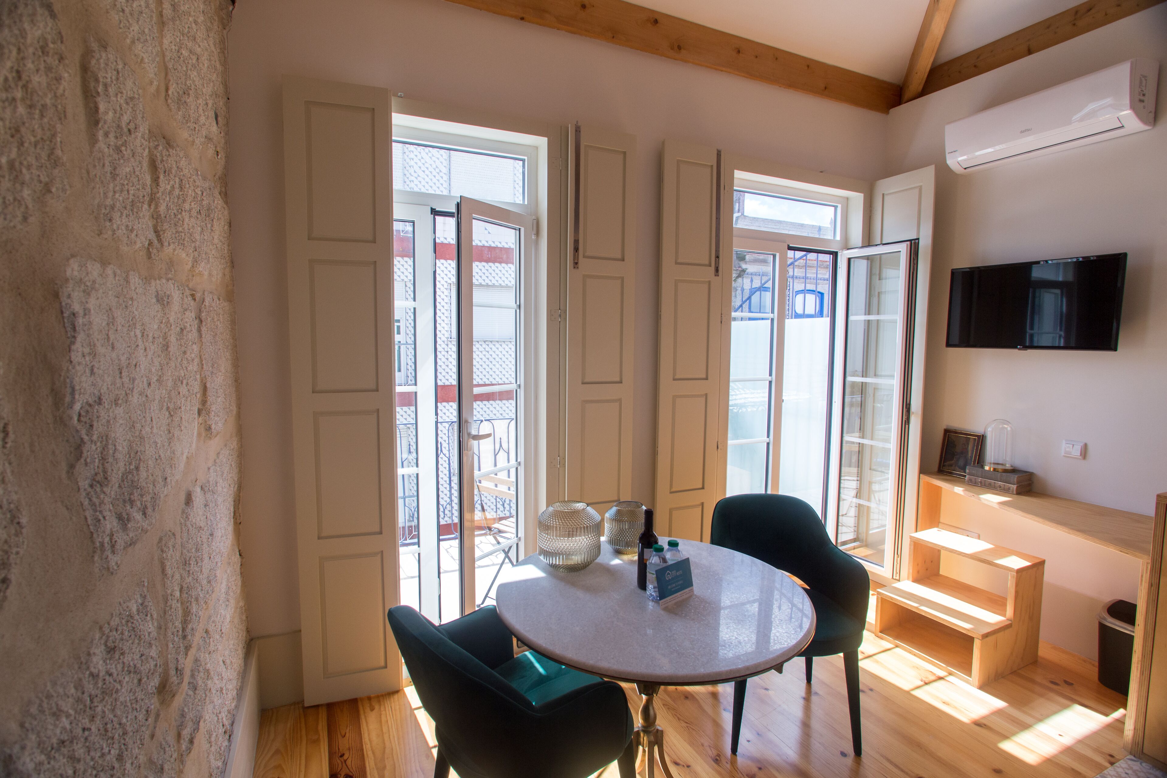 A room with a round table, two chairs, a TV mounted on the wall, and a staircase leading to an upper level.