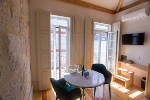 A room with a round table, two chairs, a TV mounted on the wall, and a staircase leading to an upper level.