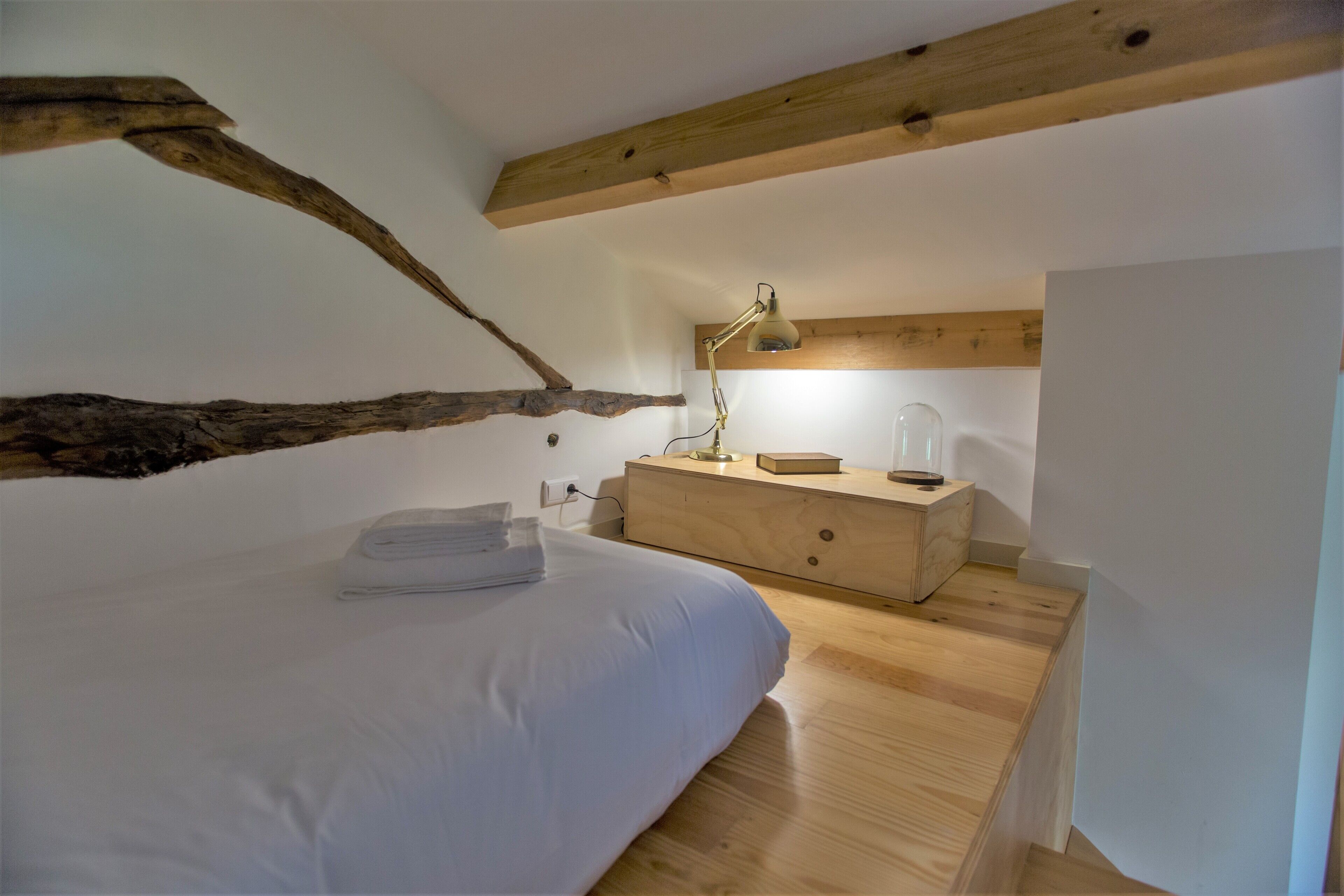 A bedroom with a bed, wooden headboard, a nightstand, a lamp, and a dresser.