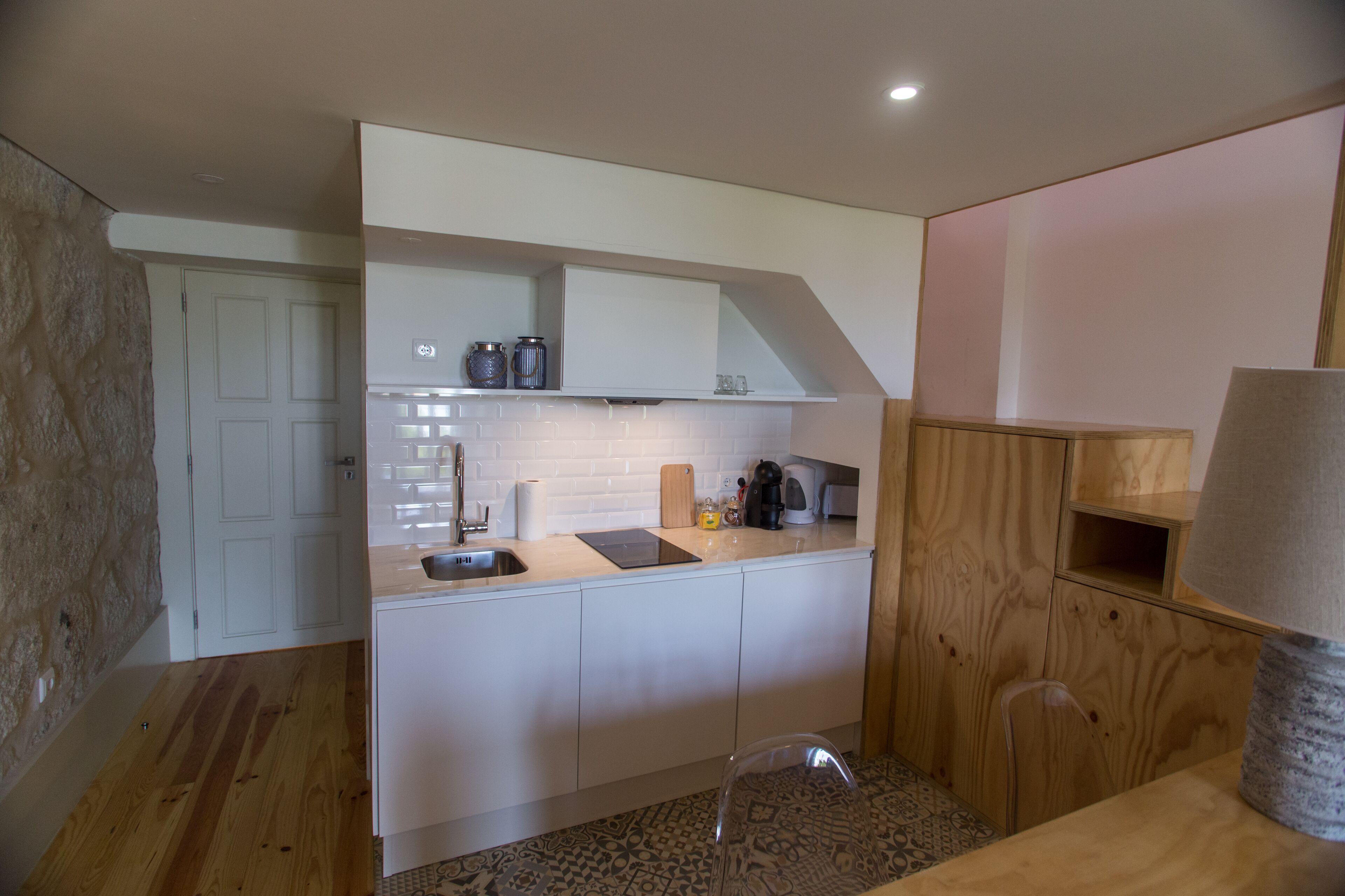 A compact kitchen with white cabinets, a countertop, a sink, and a wooden chair.