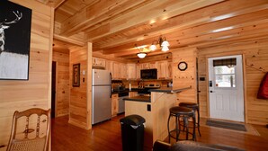 A wooden cabin interior with a kitchen, dining area, and a door with a window.