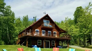 A large wooden cabin with a balcony, surrounded by a grassy lawn and trees.