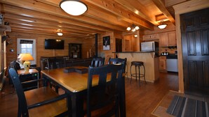 A wooden cabin interior with a dining area, kitchen, and bar.