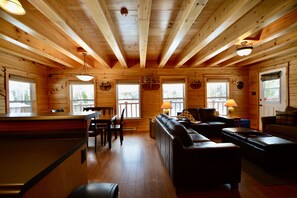 A log cabin interior with a dining area, a sofa, and a fireplace. - Cast Away Lodge… cast your worries away on the banks of the Miramichi River (Barnettville)