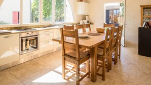 A kitchen with a large window, wooden chairs, a dining table, and a refrigerator. - L'Ancien Pigeonnier (Trebes)