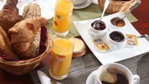 Een ontbijttafel met croissants, sinaasappelsap, koffie en jam.