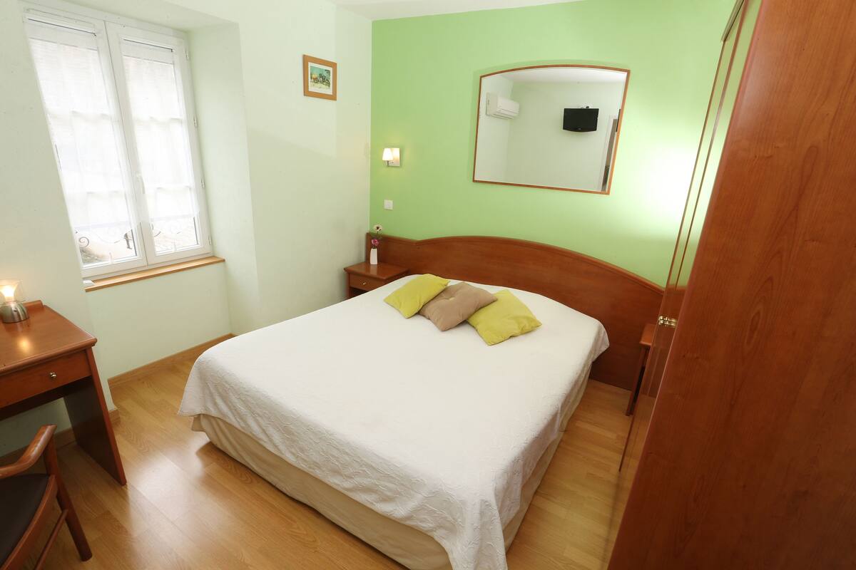 Ein Schlafzimmer mit einem Bett, einem Schreibtisch, einem Stuhl, einem Fenster und einem Spiegel.