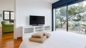 A modern hotel room with a large bed, a flat-screen TV, a green sofa, and a view of the marina. - PONENT - Modern apartment with sea views in Portocolom Free WiFi (Portocolom)