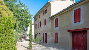 A narrow street with buildings featuring red shutters and a gravel path. - La Maison Vigneronne (Trebes)