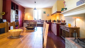 A kitchen with wooden cabinets, a dining table with chairs, a built-in oven, and a window providing natural light. - La Maison Vigneronne (Trebes)